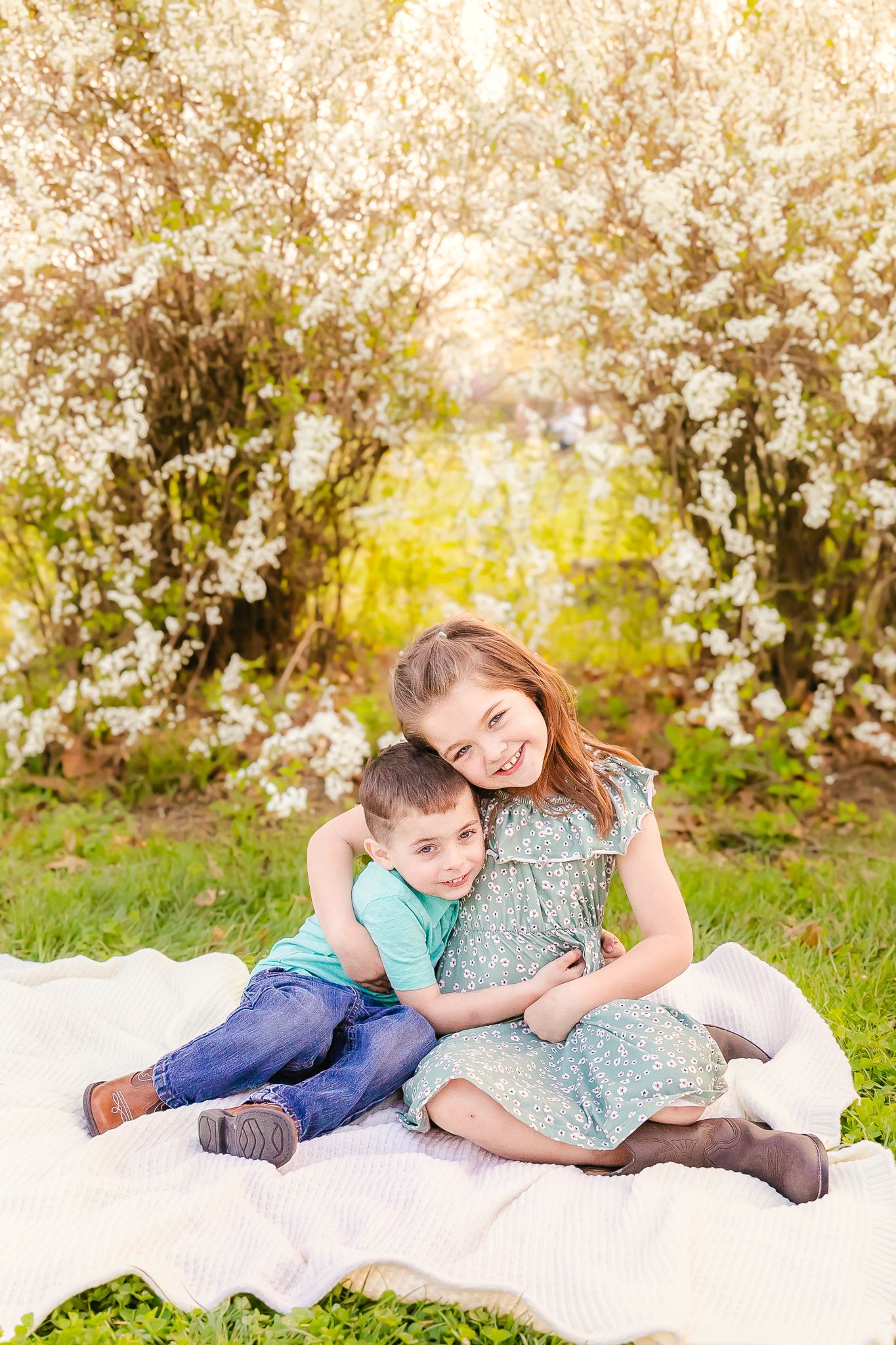 Two children sitting on a white blanket under blooming cherry blossom trees on a spring day in nature.