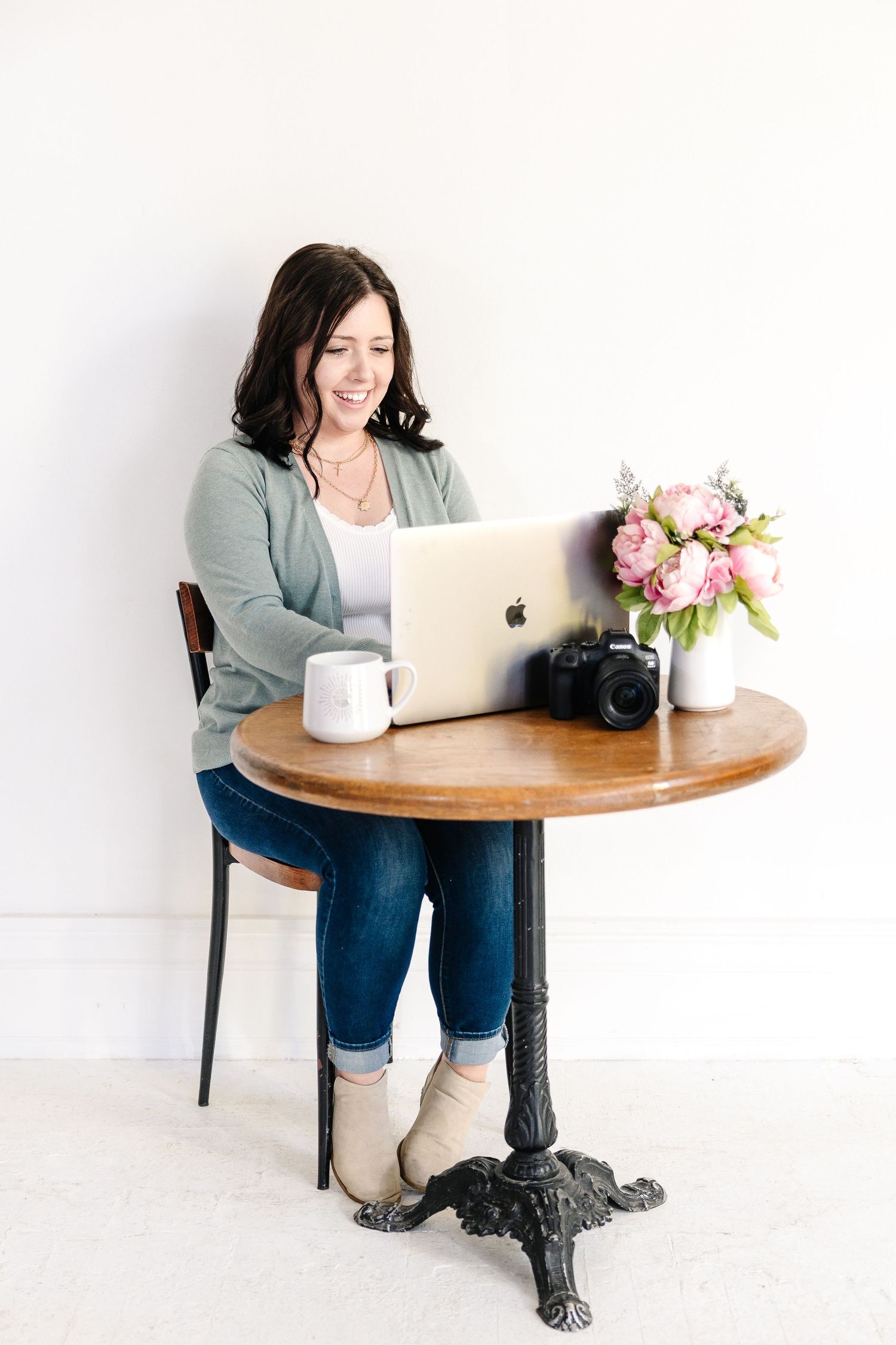A Pittsburg KS and Joplin MO brand and family works at round wooden table with laptop, camera and floral arrangement in studio.