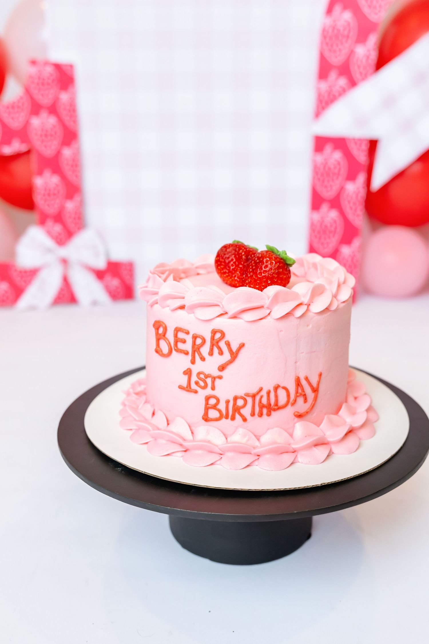 Pink strawberry-themed first birthday cake with strawberries on black cake stand for birthday photoshoot with Annie Robinson Photography.