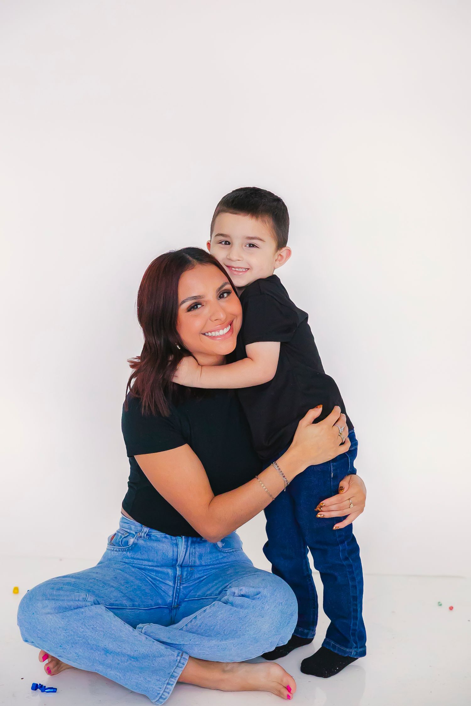 Mother and child in coordinating blue and black outfits embrace while sitting against white backdrop.
