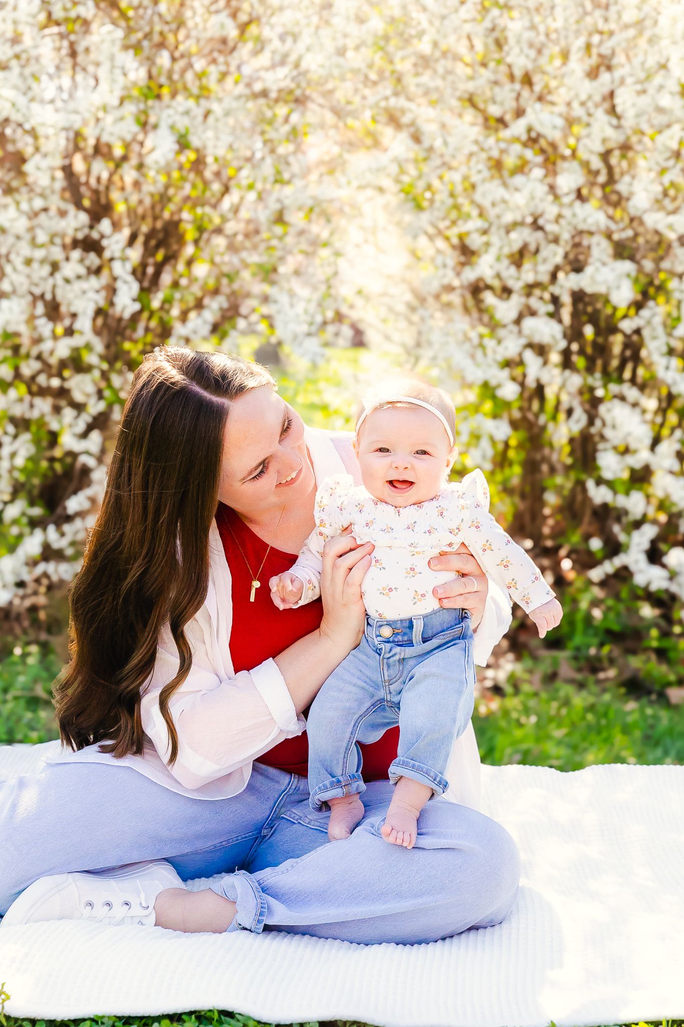 A cheerful spring scene on a white blanket under blooming cherry trees with natural sunlight filtering through for sweet mom and me photos.