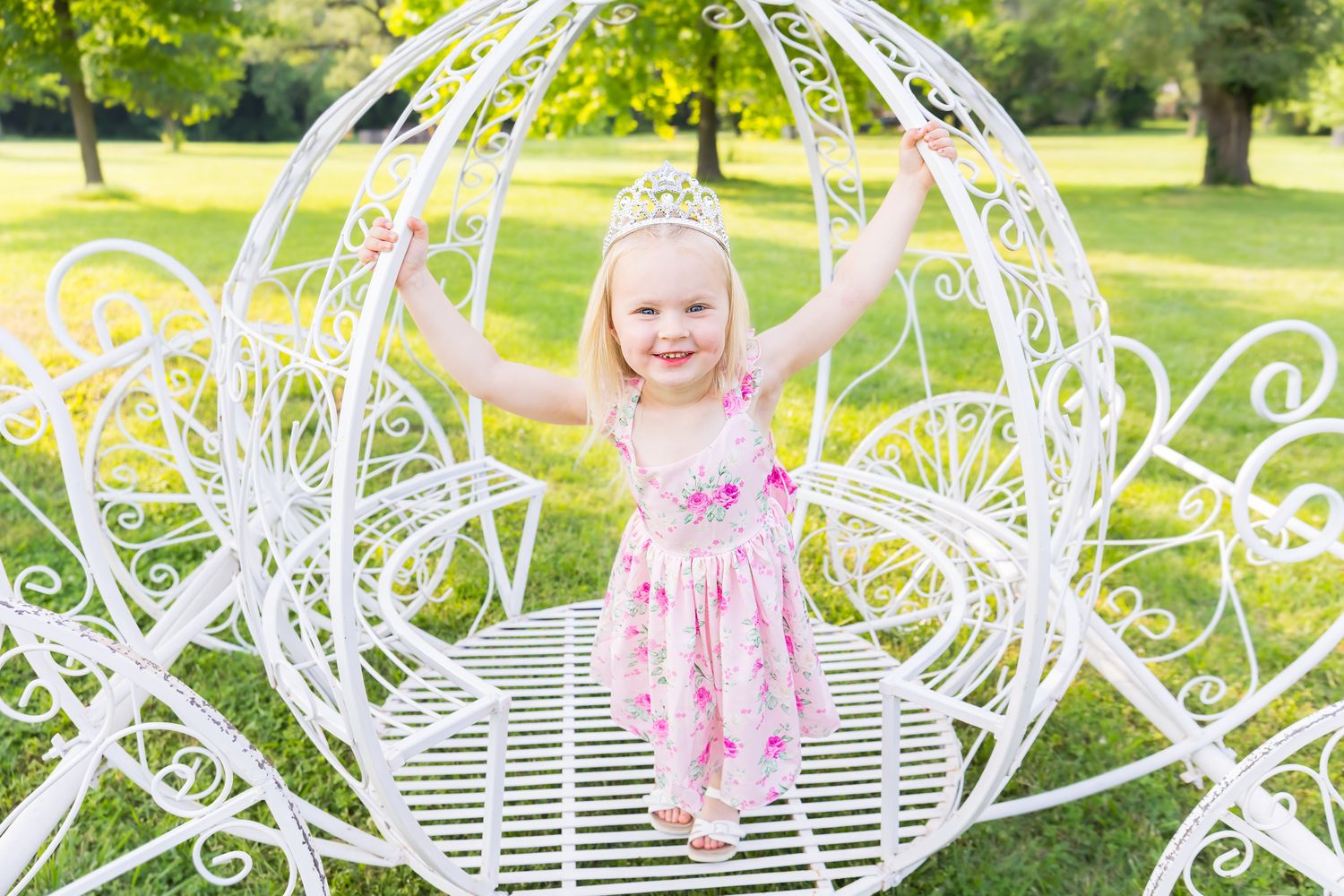 A girl stands in a white carriage with a pink dress on for smiling for a princess mini session photoshoot in Pittsburg Kansas.