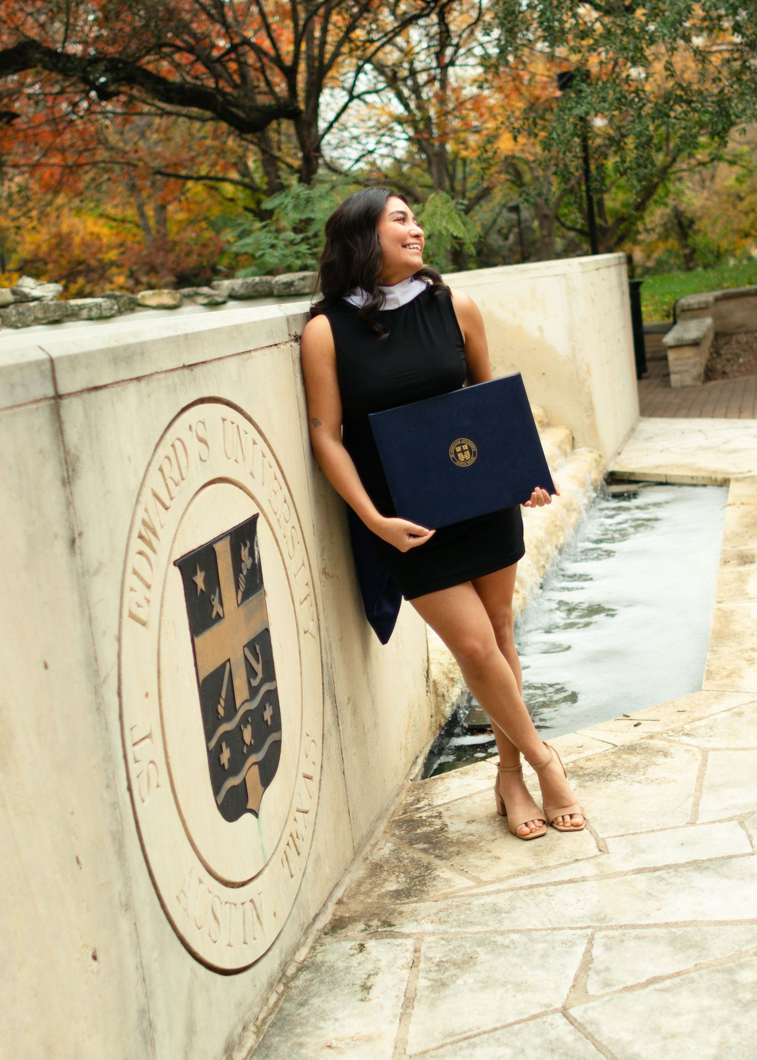 A graduating college senior holds her degree and smiles at St. Edward's University in Austin, Texas, during her senior portraits.