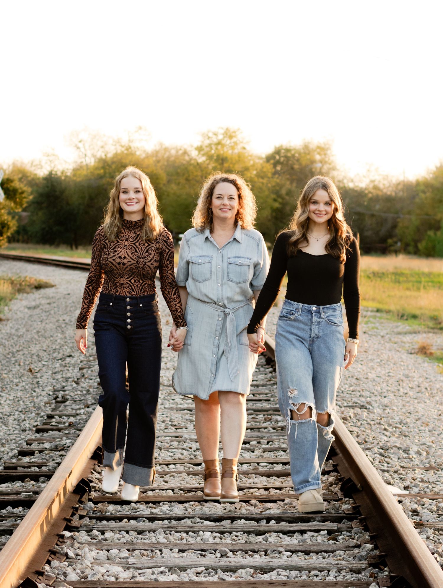 A mom and her daughters hold hands walking down an abandoned railroad track during a photo shoot in Georgetown, Texas.