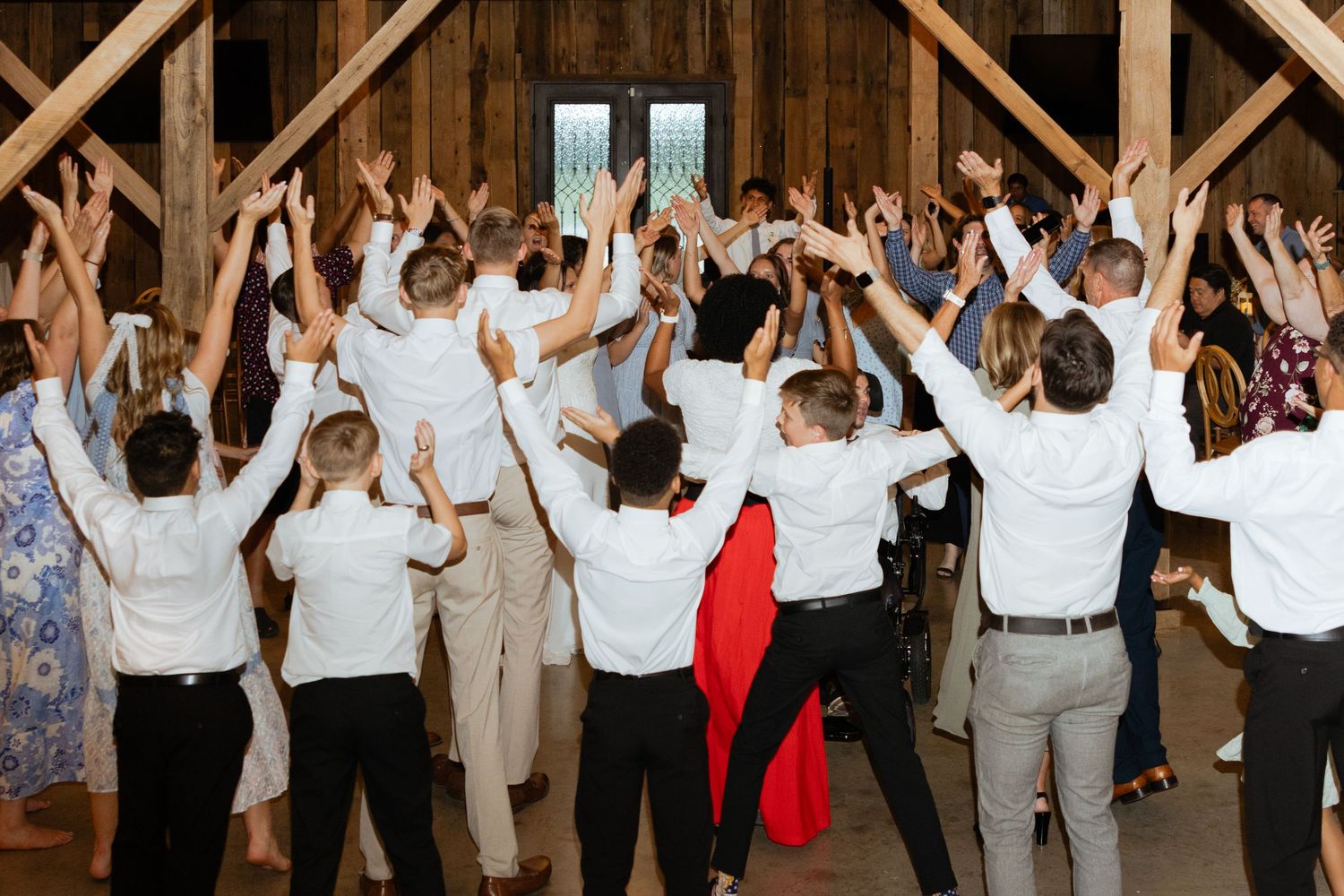 A wedding reception group holds their hands in the air collectively to a song.