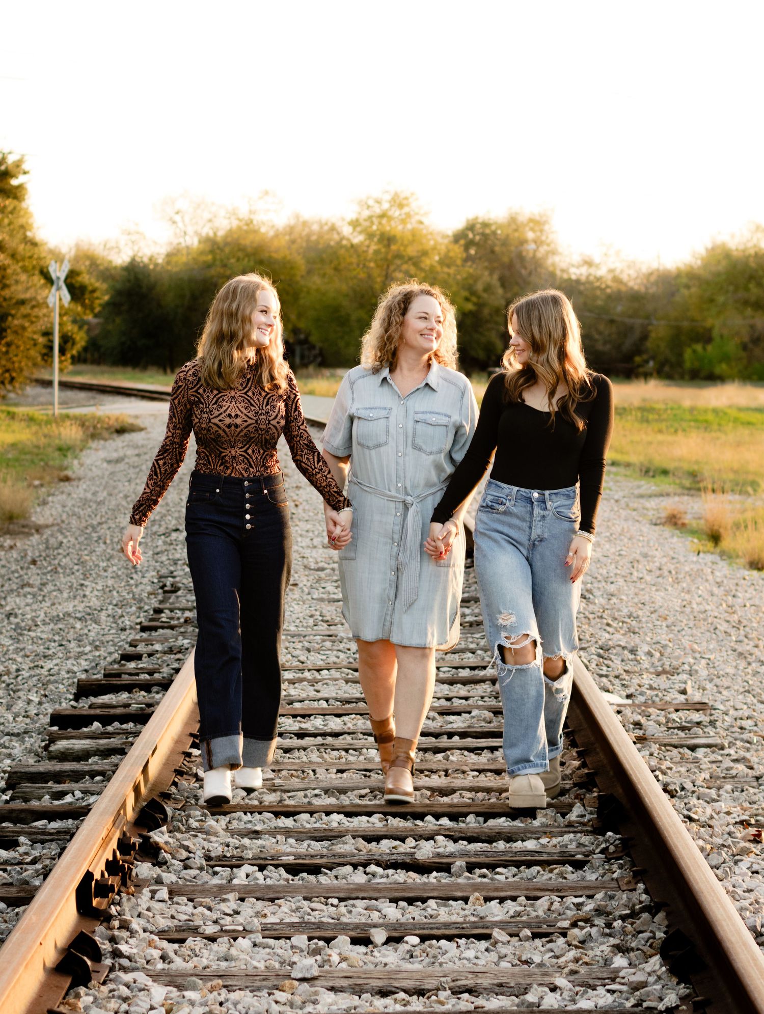 A mom and her daughters hold hands walking down an abandoned railroad track during a photo shoot in Georgetown, Texas.