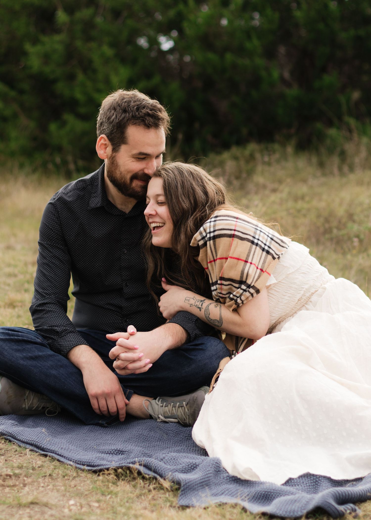 A couple sits on a blanket laughing with each other at a park near Austin, Texas.