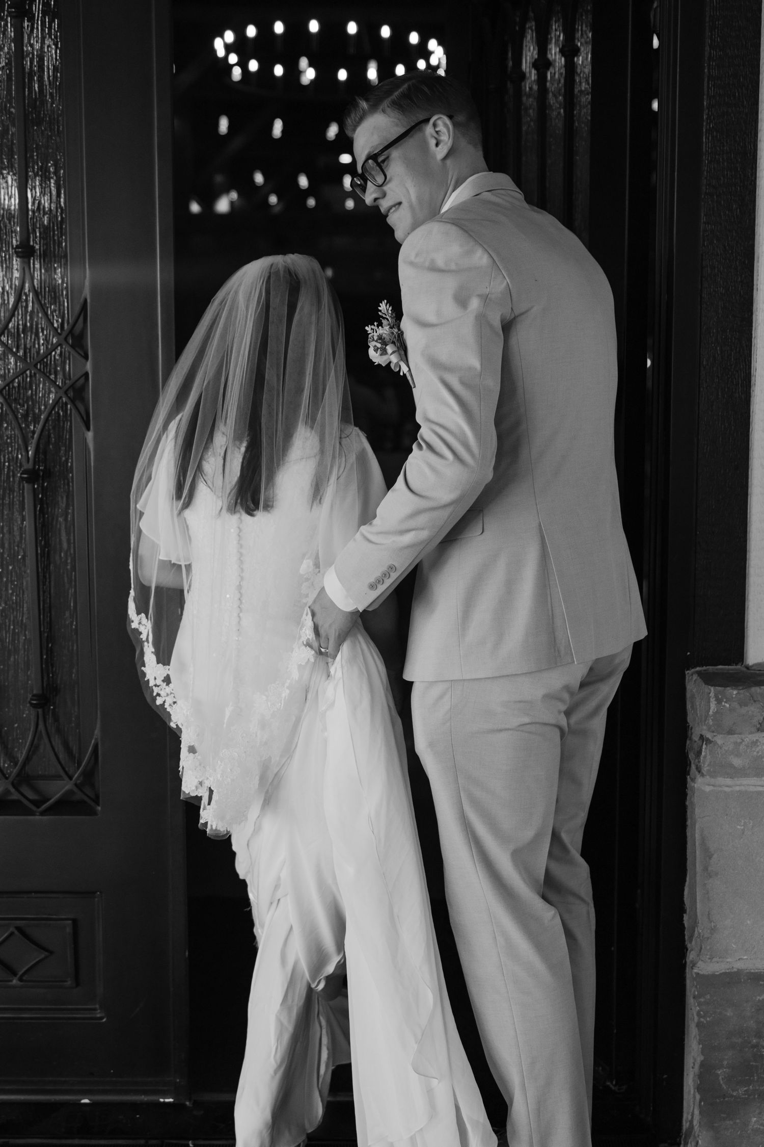 A groom holds his bride's dress as they walk into their wedding reception hall in Texas.