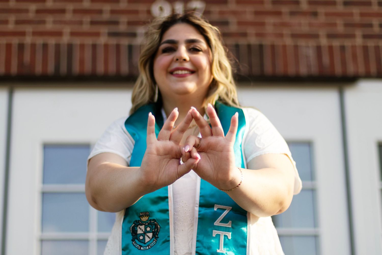 A college student creates a sorority hand sign in her graduation memorabilia on campus.