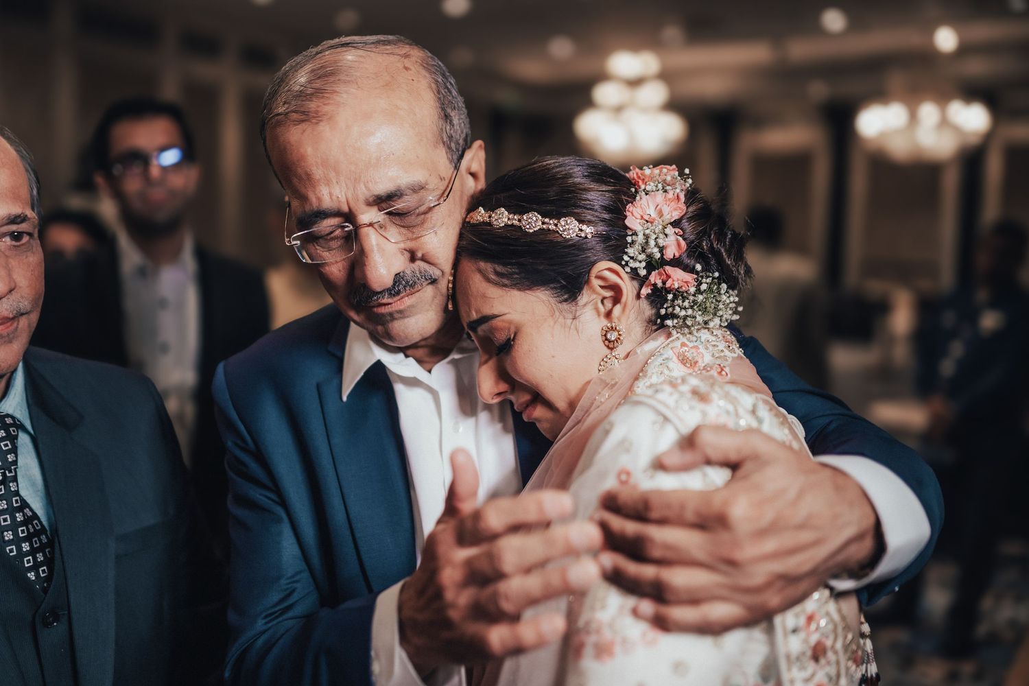 Emotional bride hugging an older man in a suit at an Indian wedding reception.