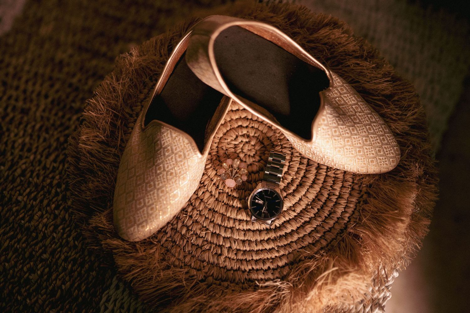 Elegant cream loafers and a wristwatch displayed on a woven straw bag with fur trim.