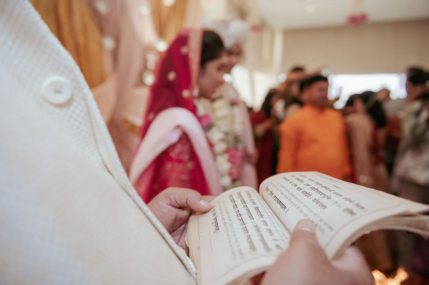Officiant reads from a sacred text during a traditional Indian wedding ceremony with bride in red dupatta.
