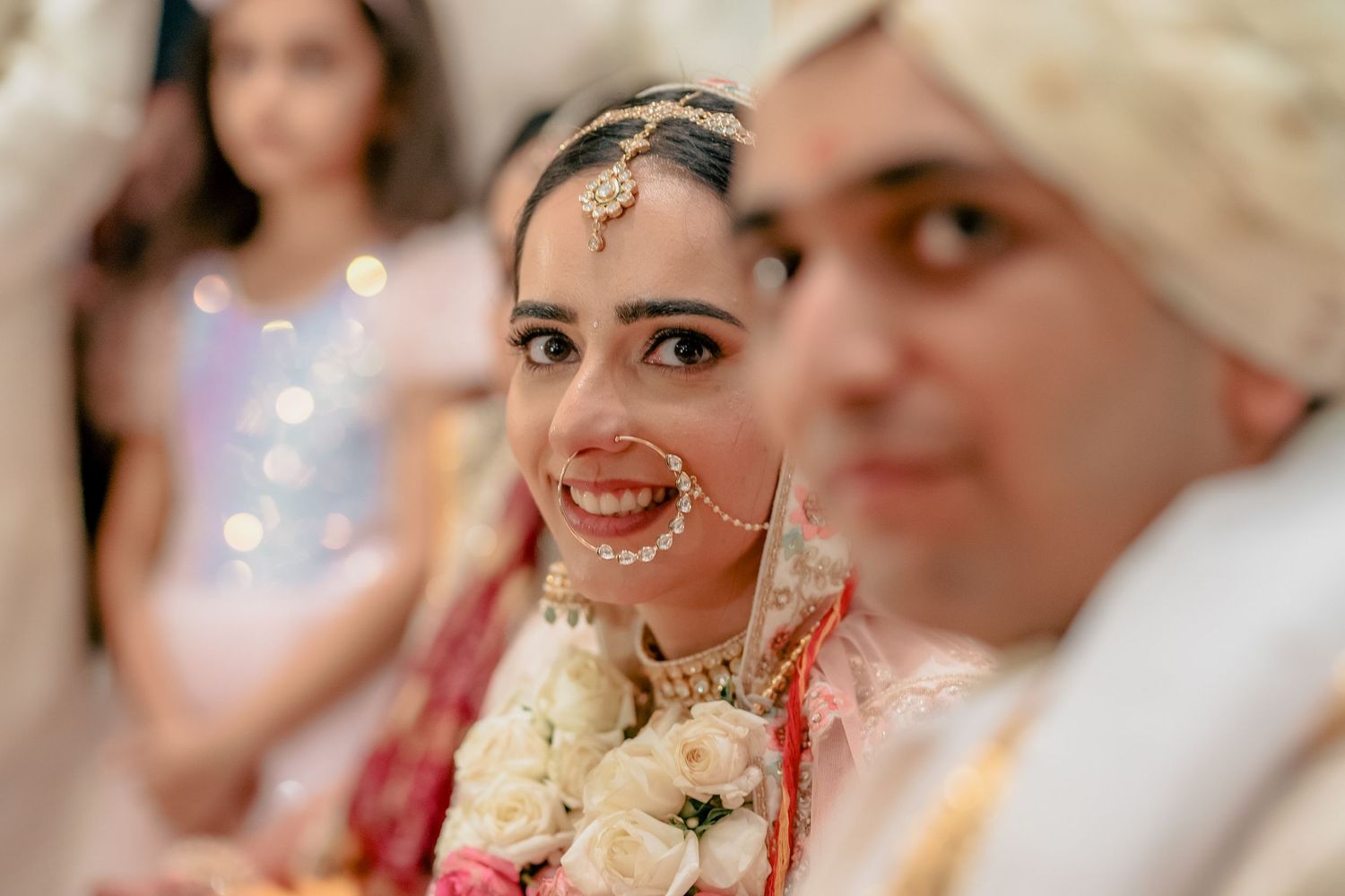 Radiant Indian bride with nose ring and floral garland smiles at wedding ceremony.