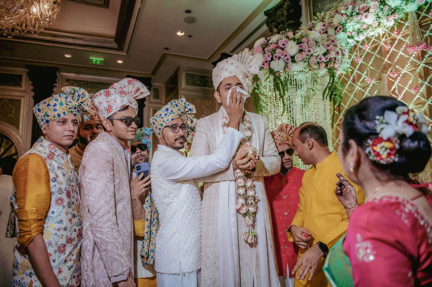 Indian groom in white sherwani emotional during wedding ceremony surrounded by family and friends.