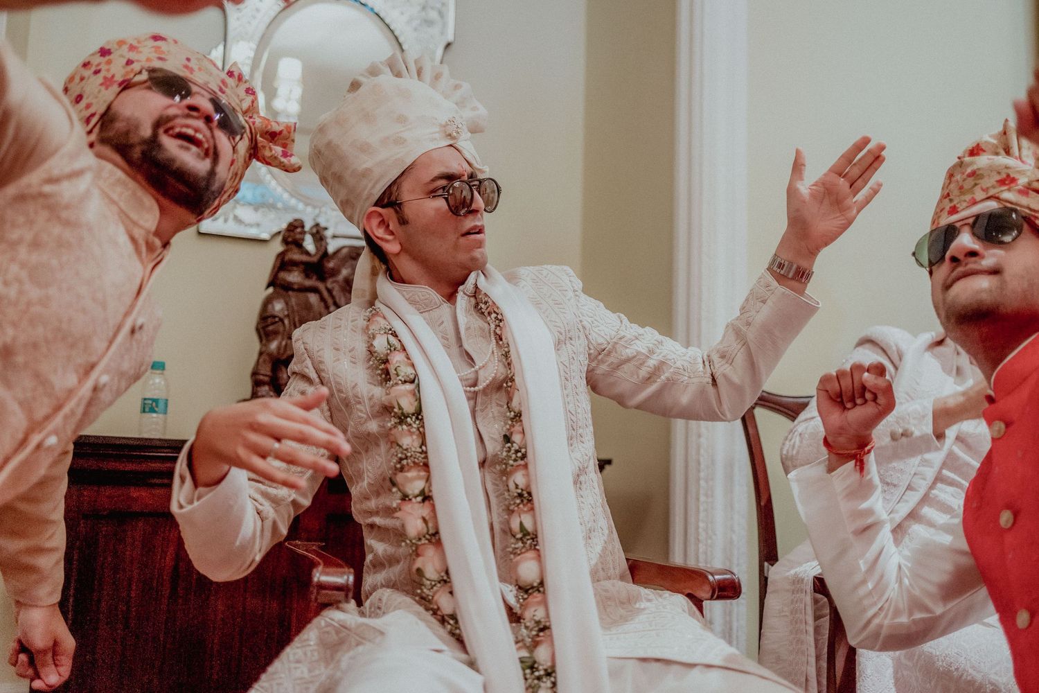 Groom in white sherwani celebrates joyfully with groomsmen in matching turbans at wedding.