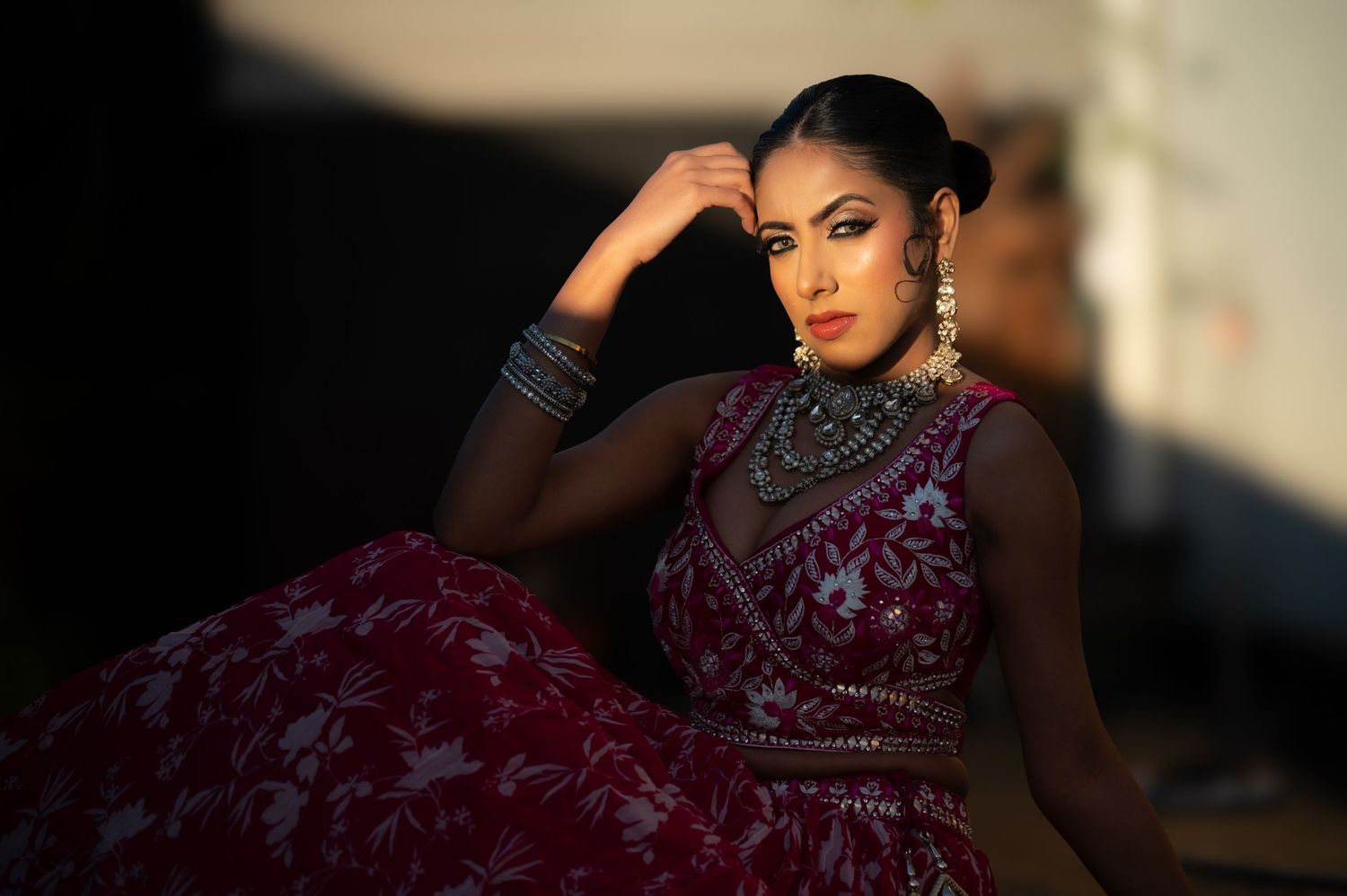 South Asian bride in maroon floral lehenga with silver jewelry poses in golden outdoor light.