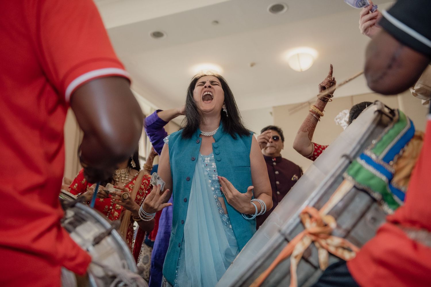 Woman in blue saree singing passionately near musicians at Indian wedding celebration.