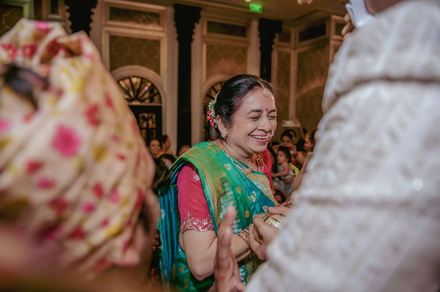 Joyful woman in green and pink saree clapping and smiling during Indian wedding celebration.