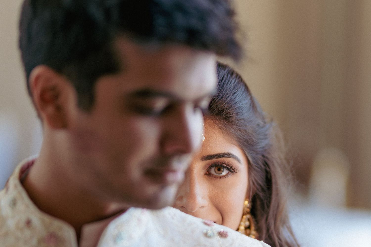 Close-up portrait of Indian bride peeking over grooms shoulder with gold nose ring and jewelry.