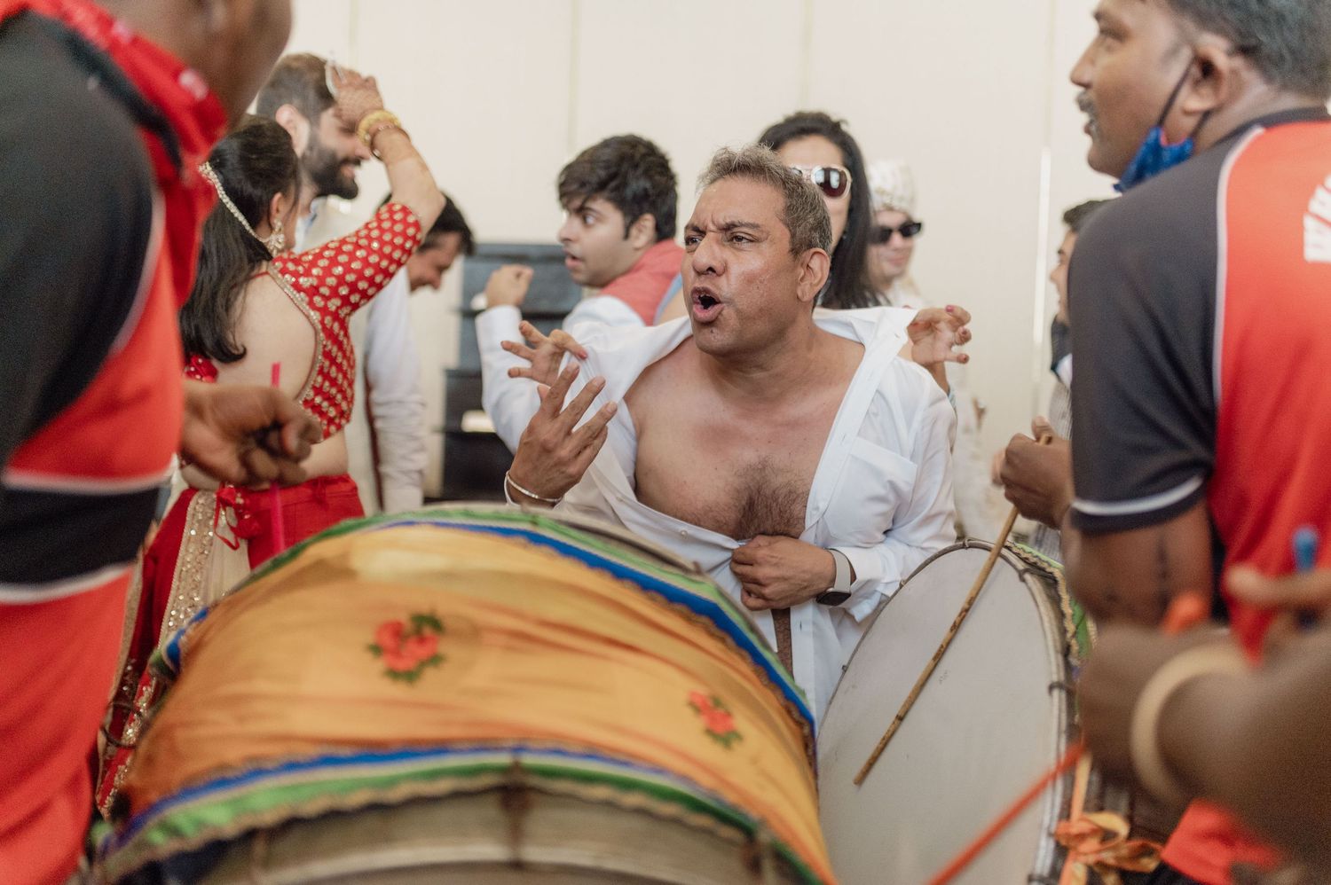 Shirtless dhol player performing energetically at traditional Indian wedding music ceremony.