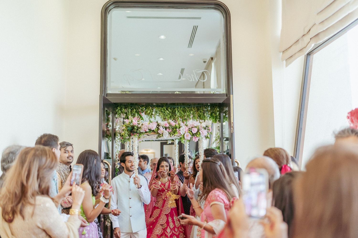 Guests photograph Indian bride and groom making elegant entrance at traditional wedding ceremony.
