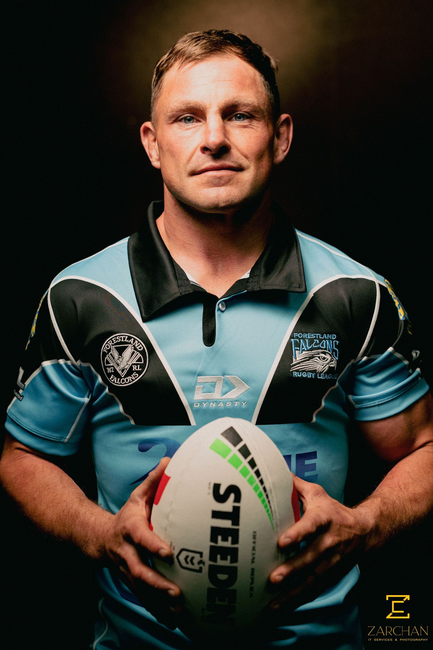 Rugby league player in blue jersey holds a Steeden football in a dramatic studio portrait.