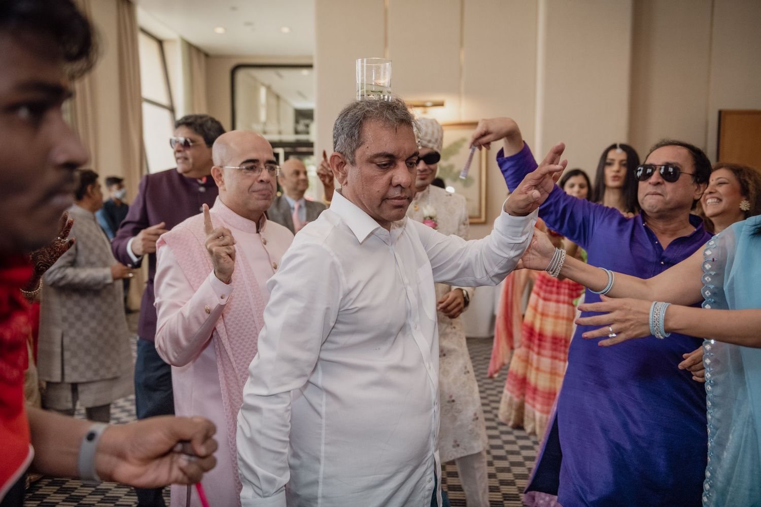Guests in traditional Indian attire dance joyfully together at a festive wedding celebration.