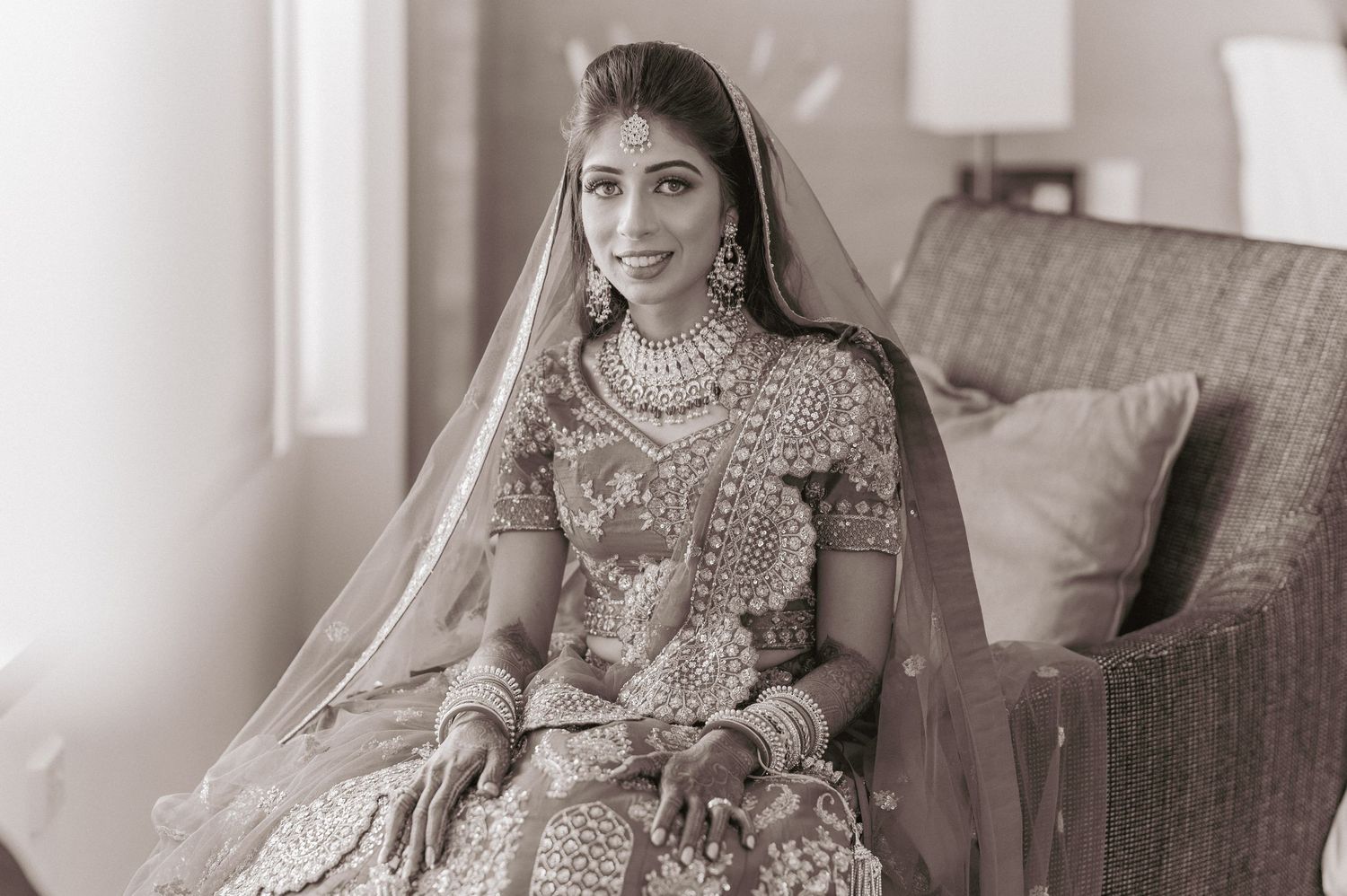 Elegant Indian bride in red lehenga poses in black and white portrait photo.