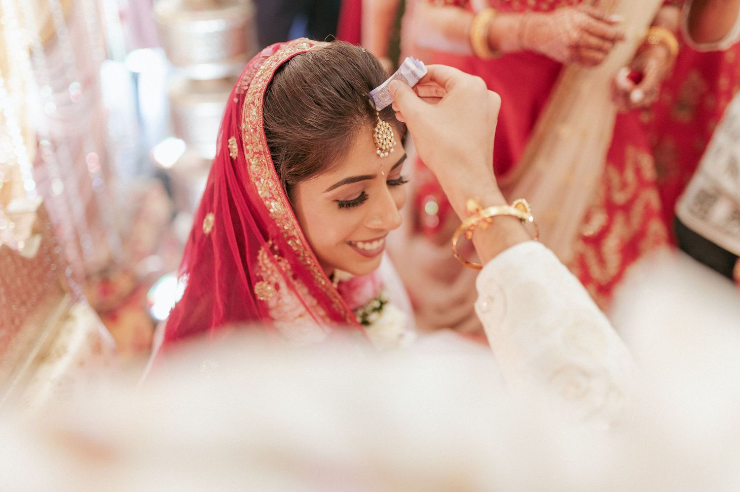 Indian groom applies sindoor to smiling bride in red bridal attire during Hindu wedding ritual.