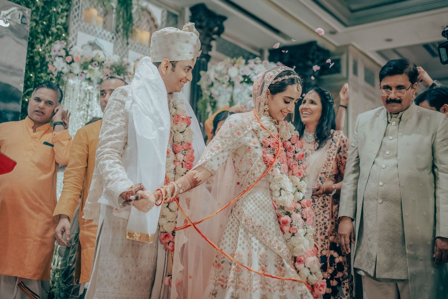Indian bride and groom perform traditional wedding ritual with red thread and flowers.