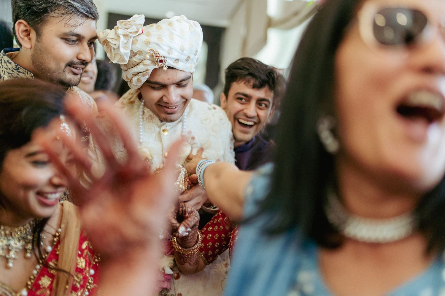 Groom in white sherwani celebrates joyfully with guests at vibrant Indian wedding.