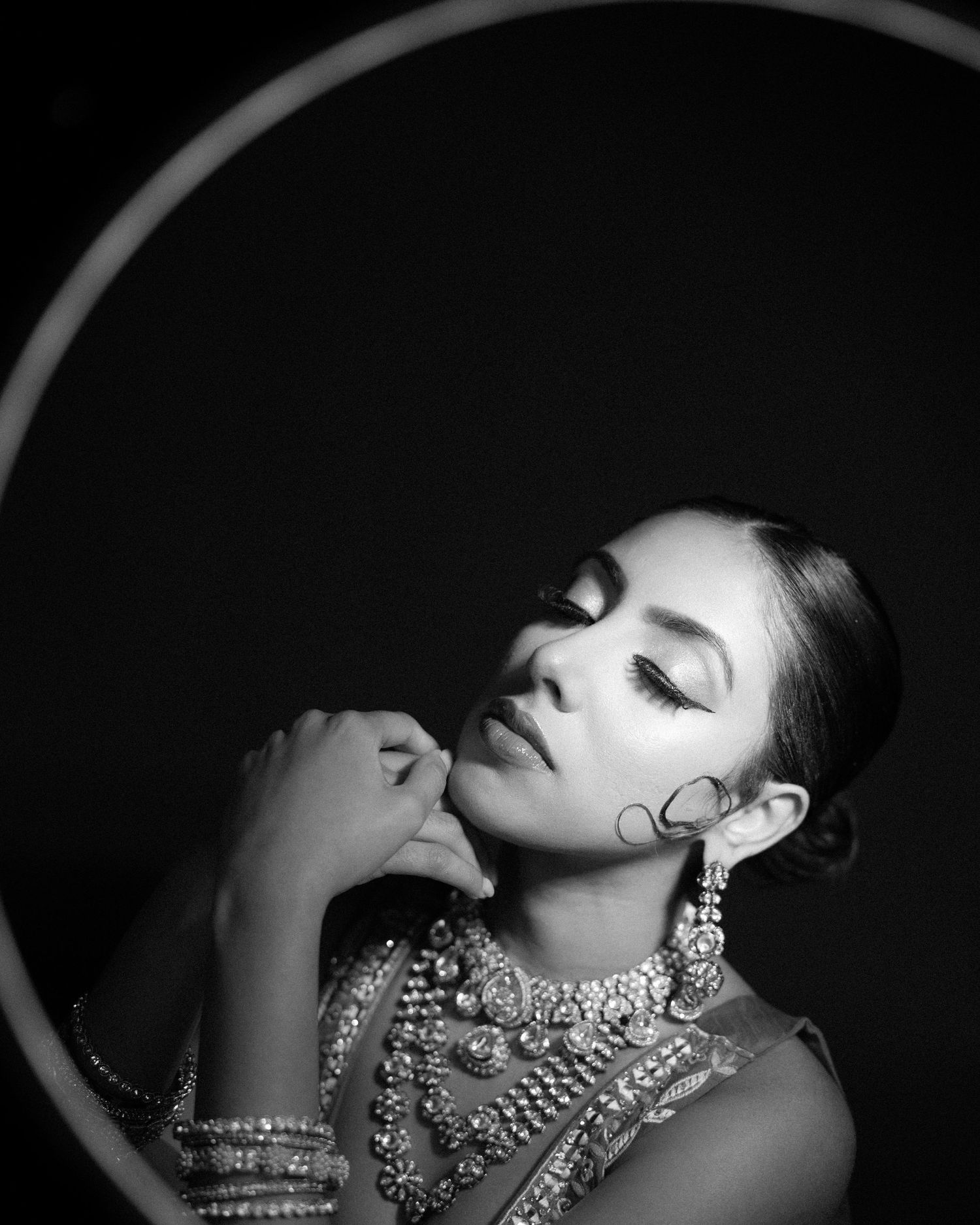 Black and white portrait of South Asian bride in ornate jewelry posing inside circular frame.