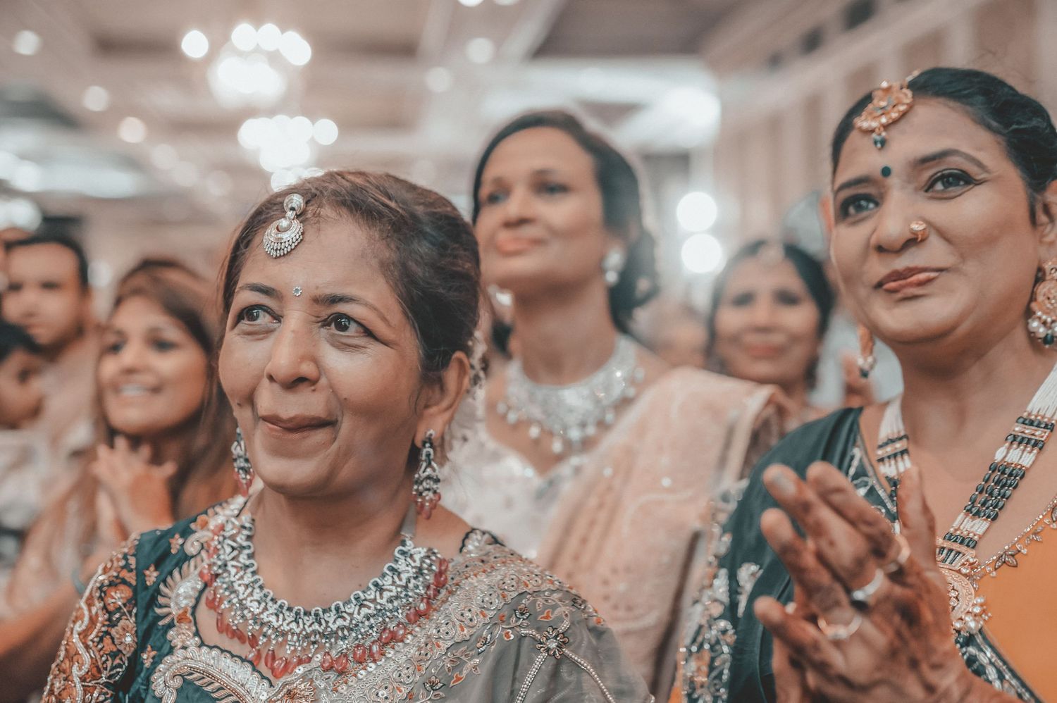 Elegantly dressed Indian wedding guests in traditional attire clapping and celebrating at a wedding ceremony.