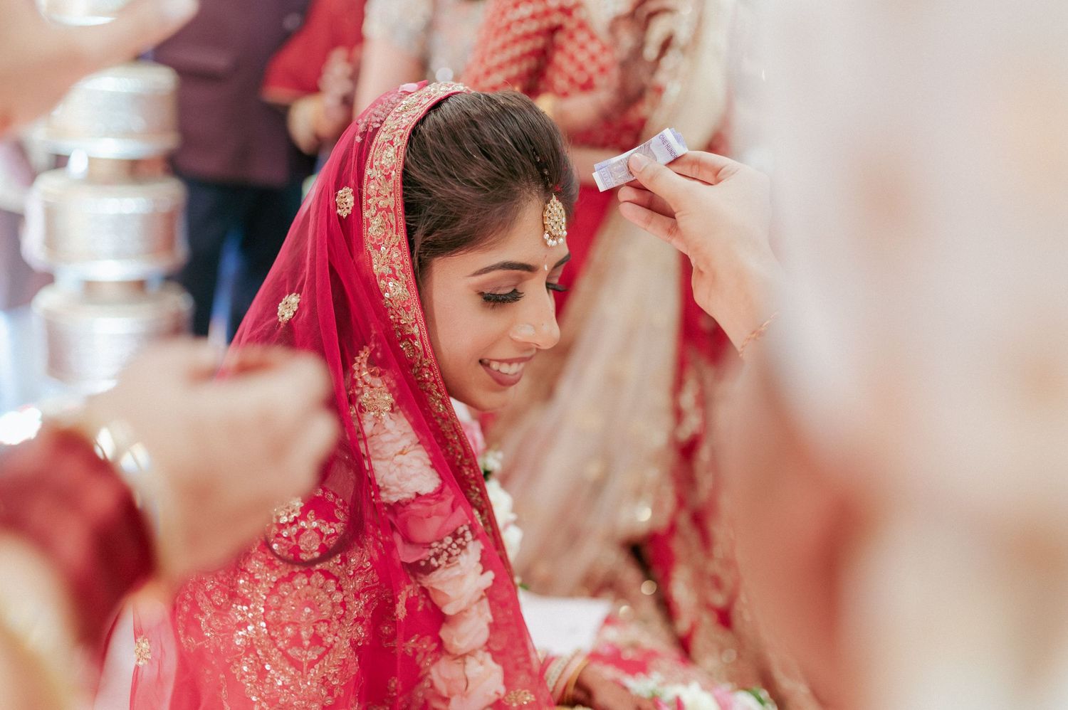 Radiant Indian bride in red dupatta smiles as groom performs sindoor ceremony during traditional Hindu wedding.