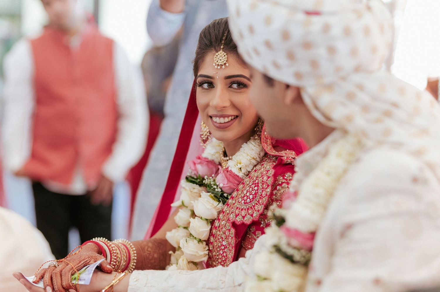 Smiling Indian bride in red lehenga and gold jewelry during traditional Hindu wedding ceremony.