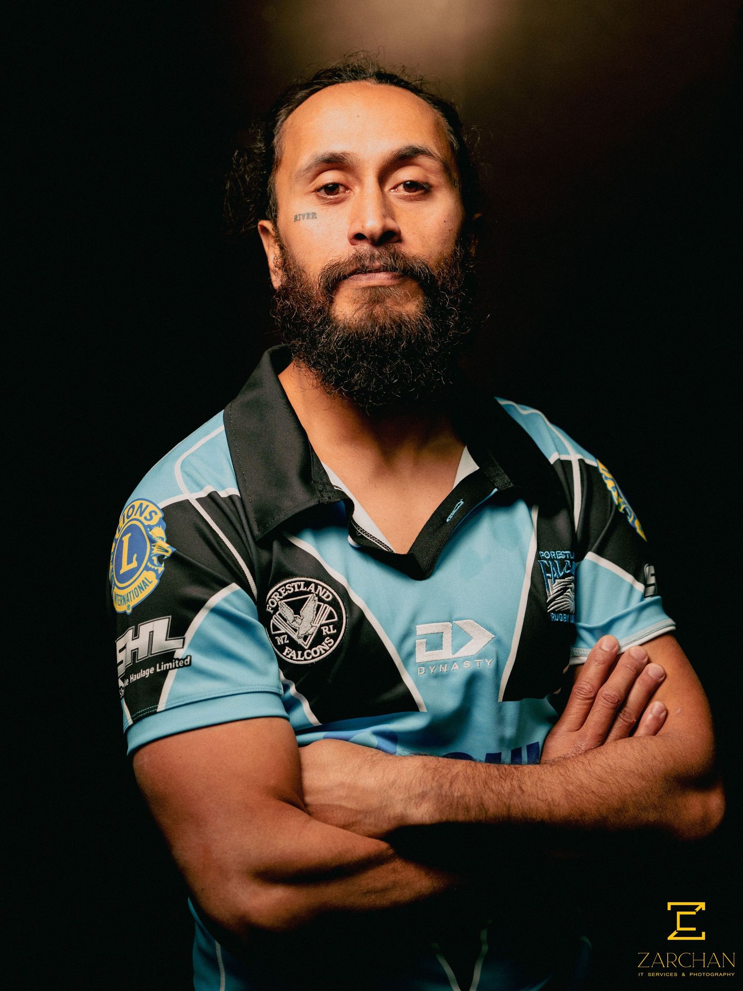 Bearded rugby league player in blue jersey poses with arms crossed in a studio portrait.