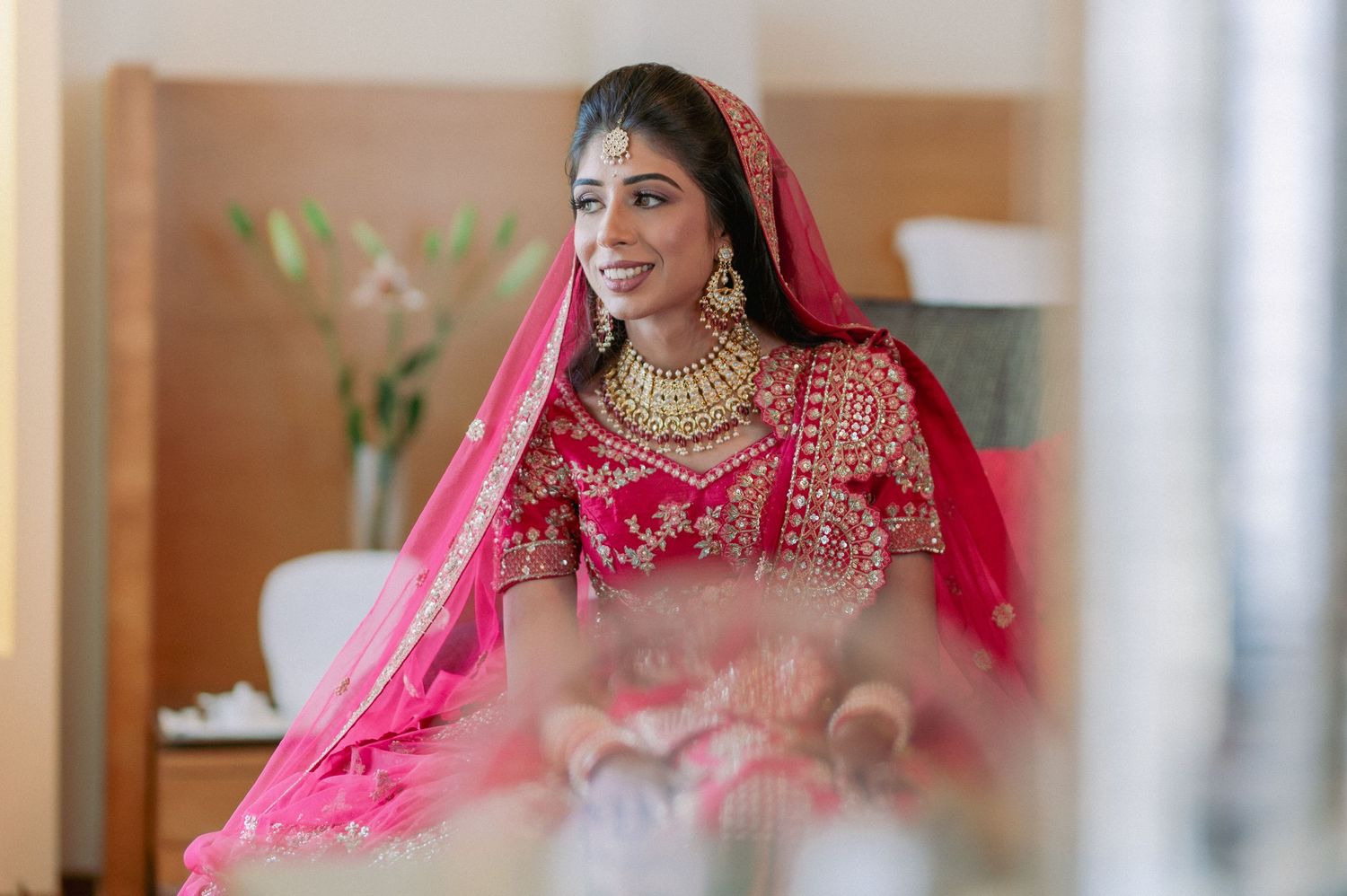 Radiant Indian bride in pink lehenga and gold jewelry smiles during wedding day.