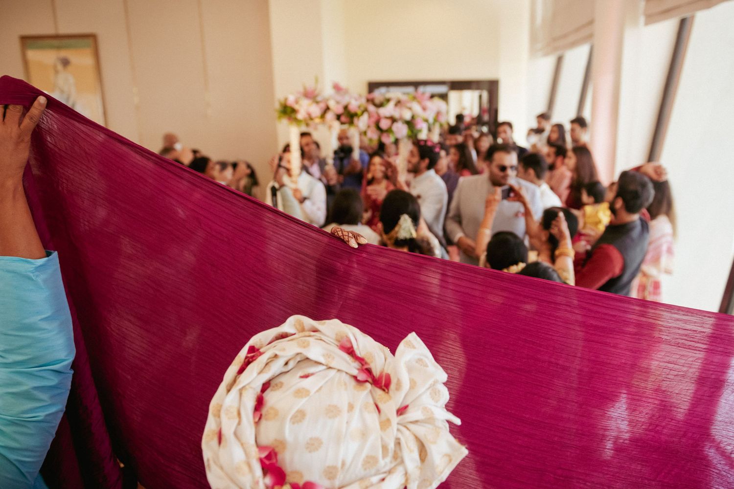 Magenta fabric held up as guests gather in background at traditional Indian wedding ceremony.