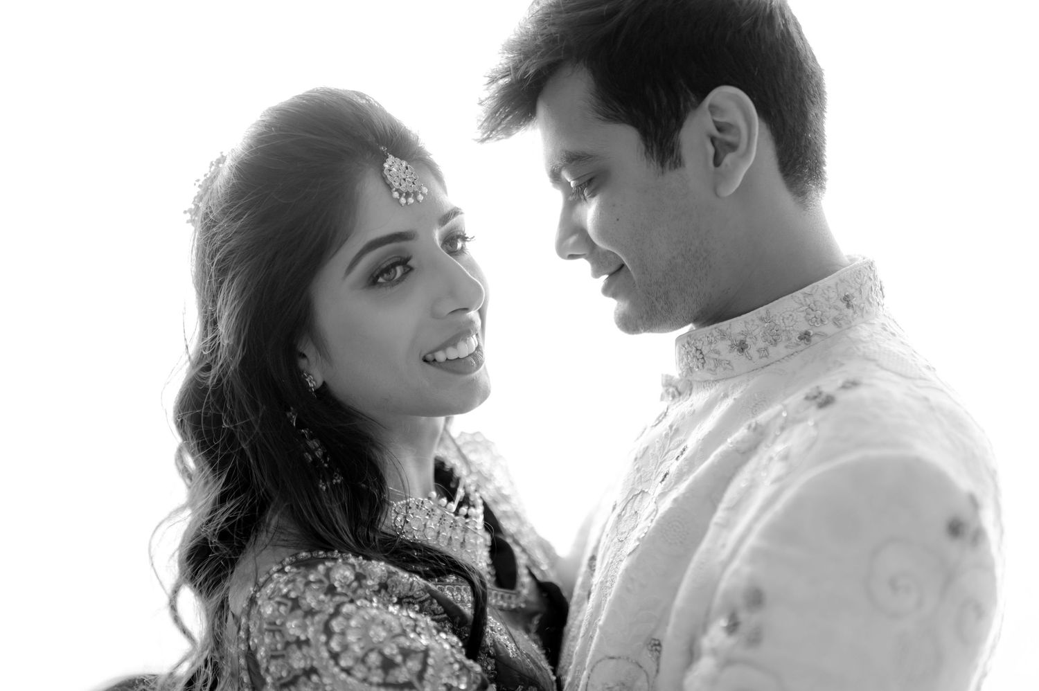 Black and white portrait of an Indian couple in traditional wedding attire, sharing a tender moment.