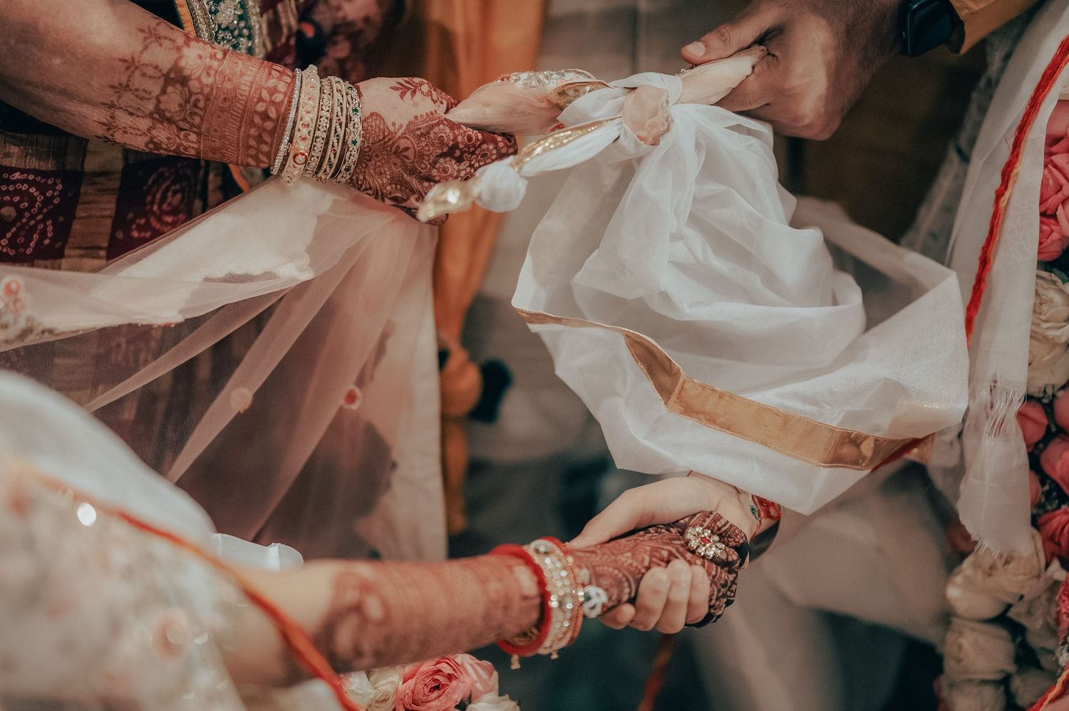 Close-up of hands during sacred Indian wedding ritual with mehndi and traditional bangles.
