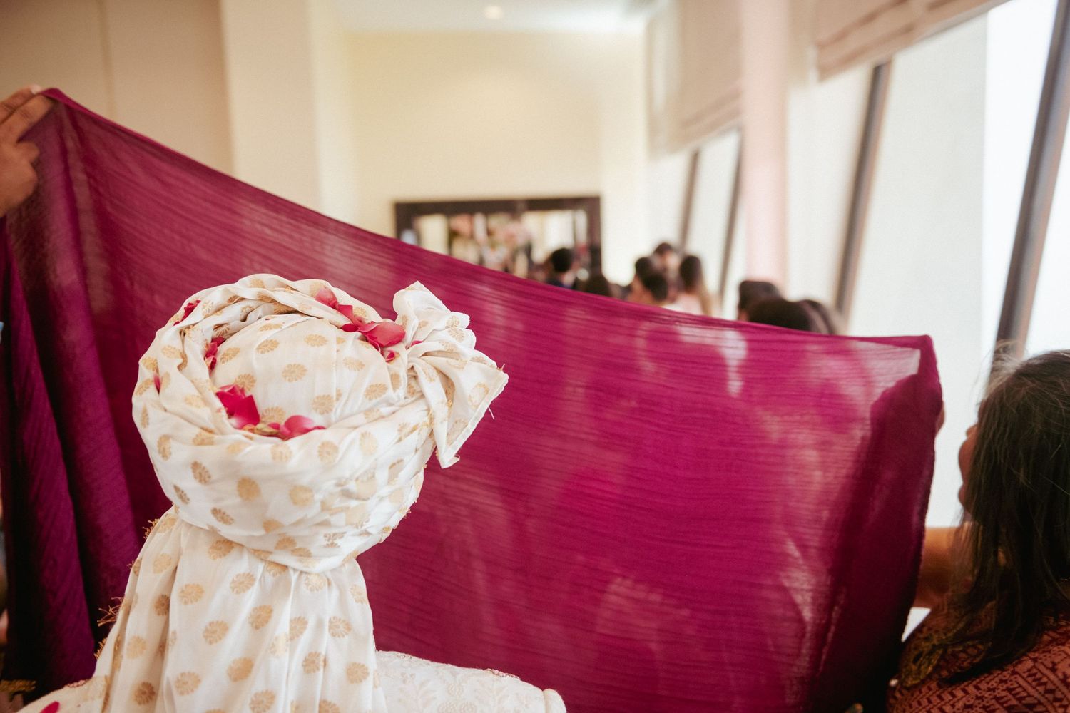 Magenta dupatta and white embroidered fabric held up during traditional Indian wedding ritual.