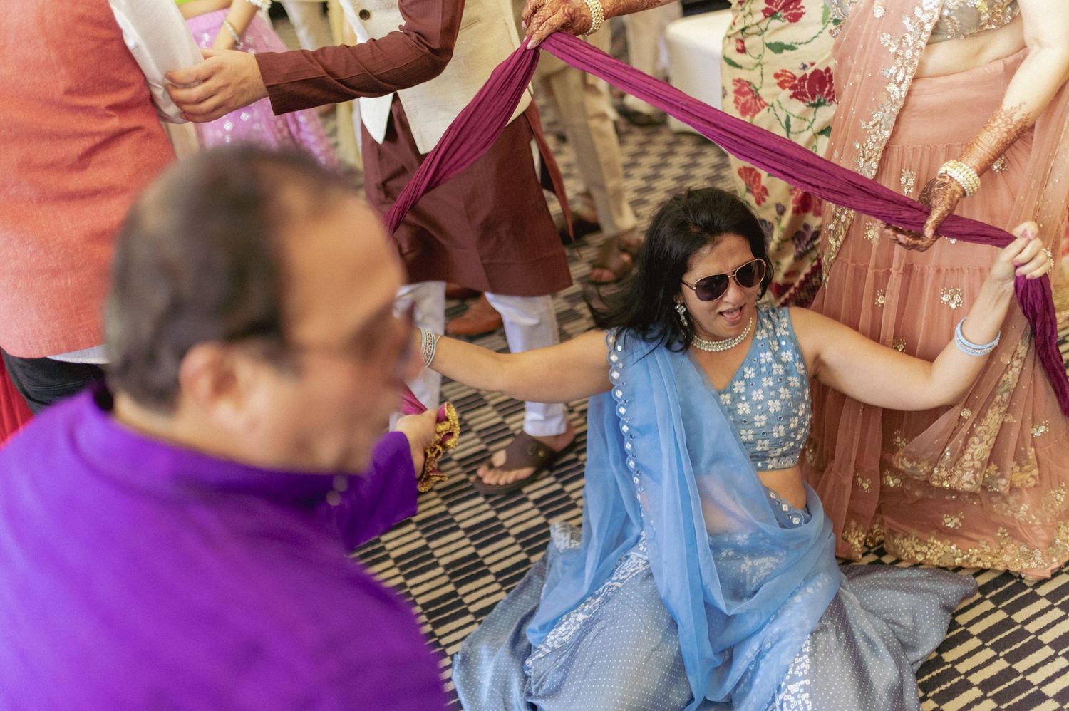 Woman in blue saree playfully holds pink dupatta during Indian wedding celebration.