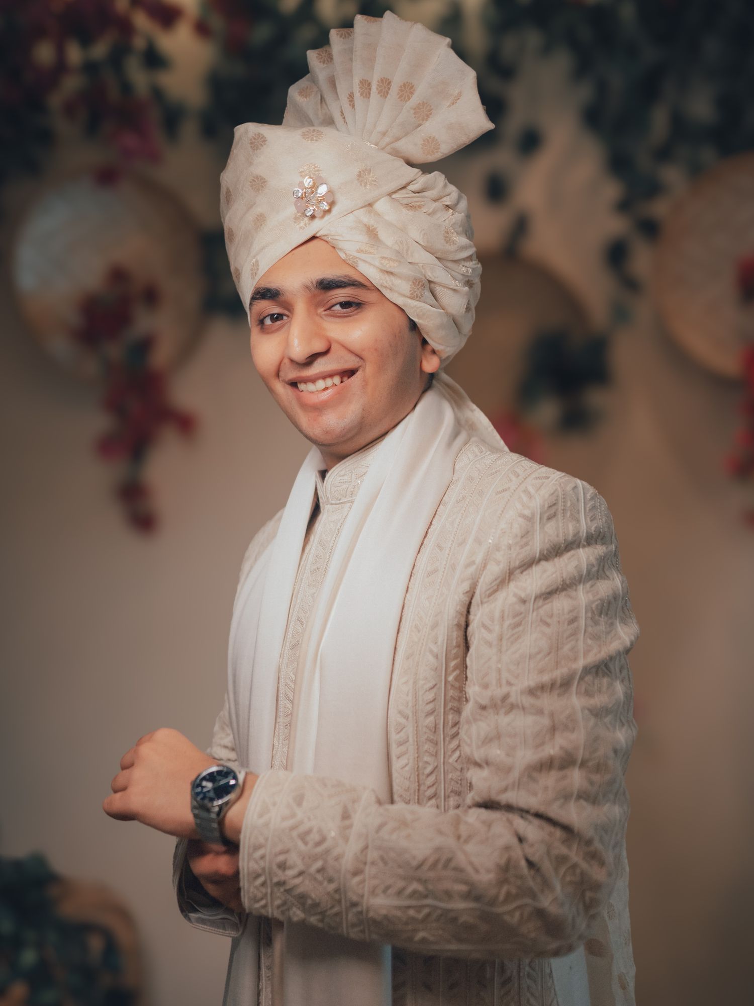 A handsome Indian groom smiles in a cream sherwani and traditional white safa turban.