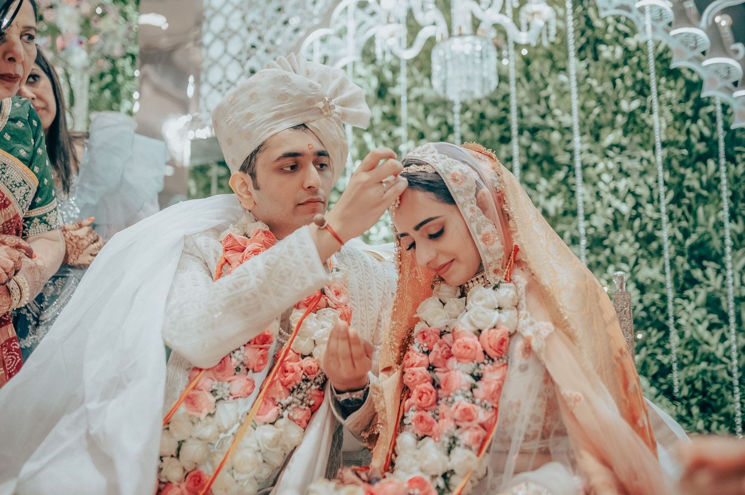 Indian groom applies sindoor to brides hair parting during traditional Hindu wedding ceremony.