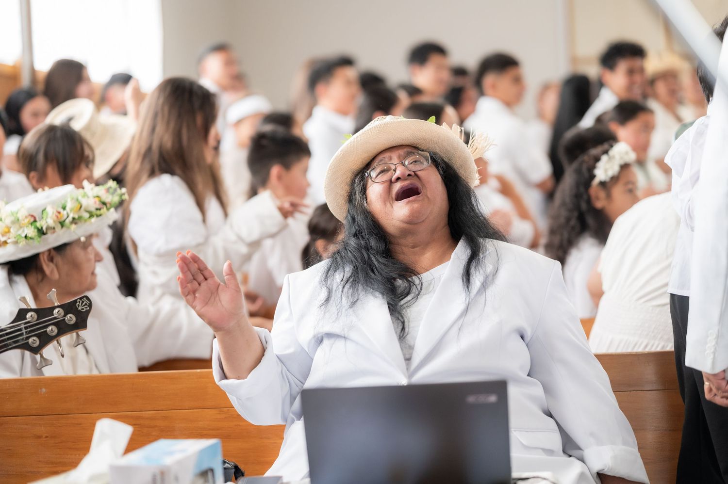 Woman in white outfit and hat laughing joyfully during a church gathering or religious ceremony.