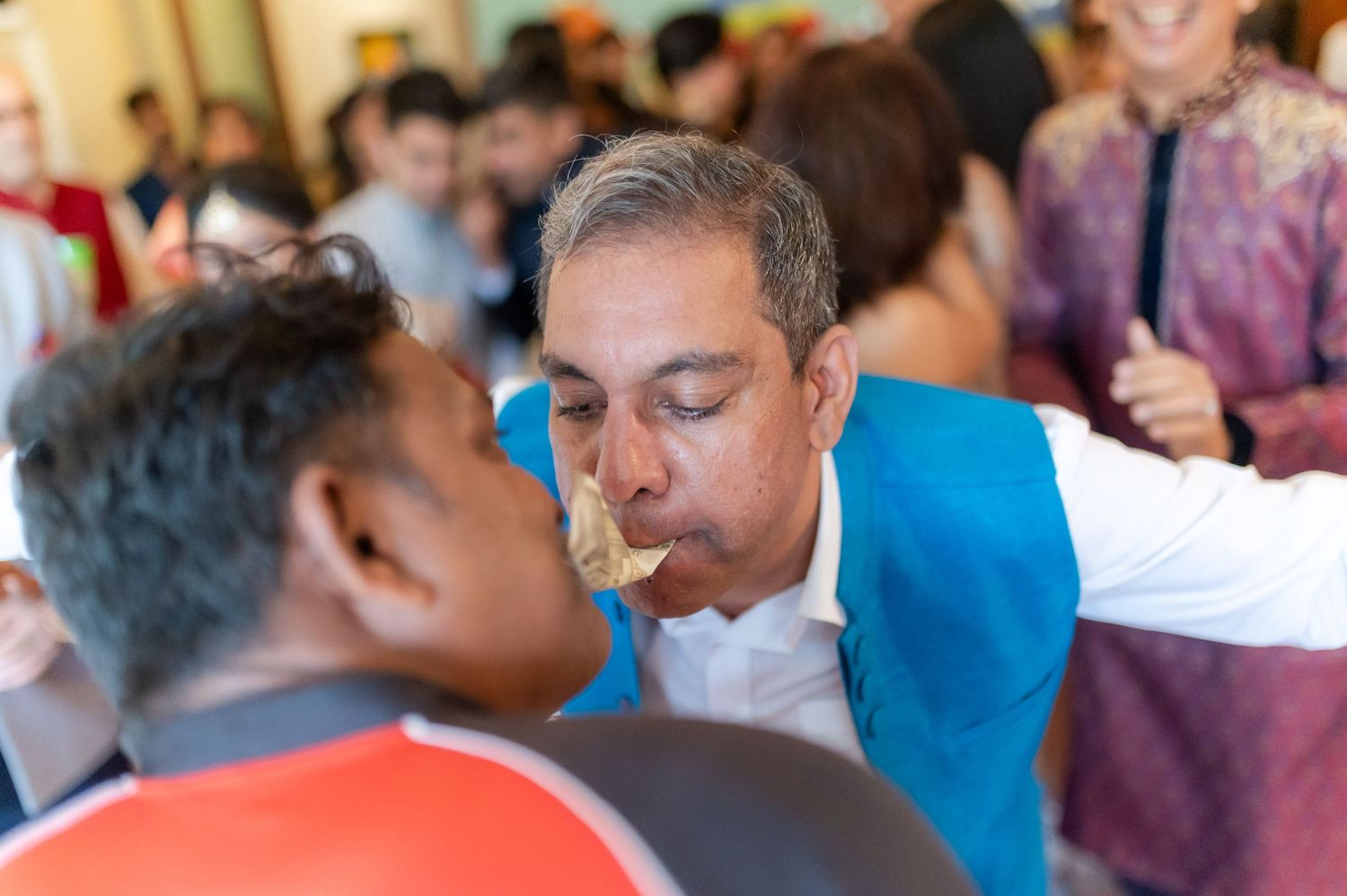 Man in blue jacket participating in a traditional cultural ceremony at a festive gathering.