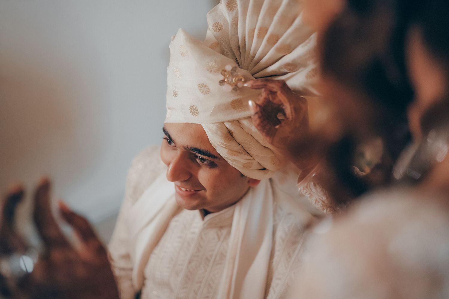 An Indian groom in a cream turban smiles softly during his traditional wedding ceremony.