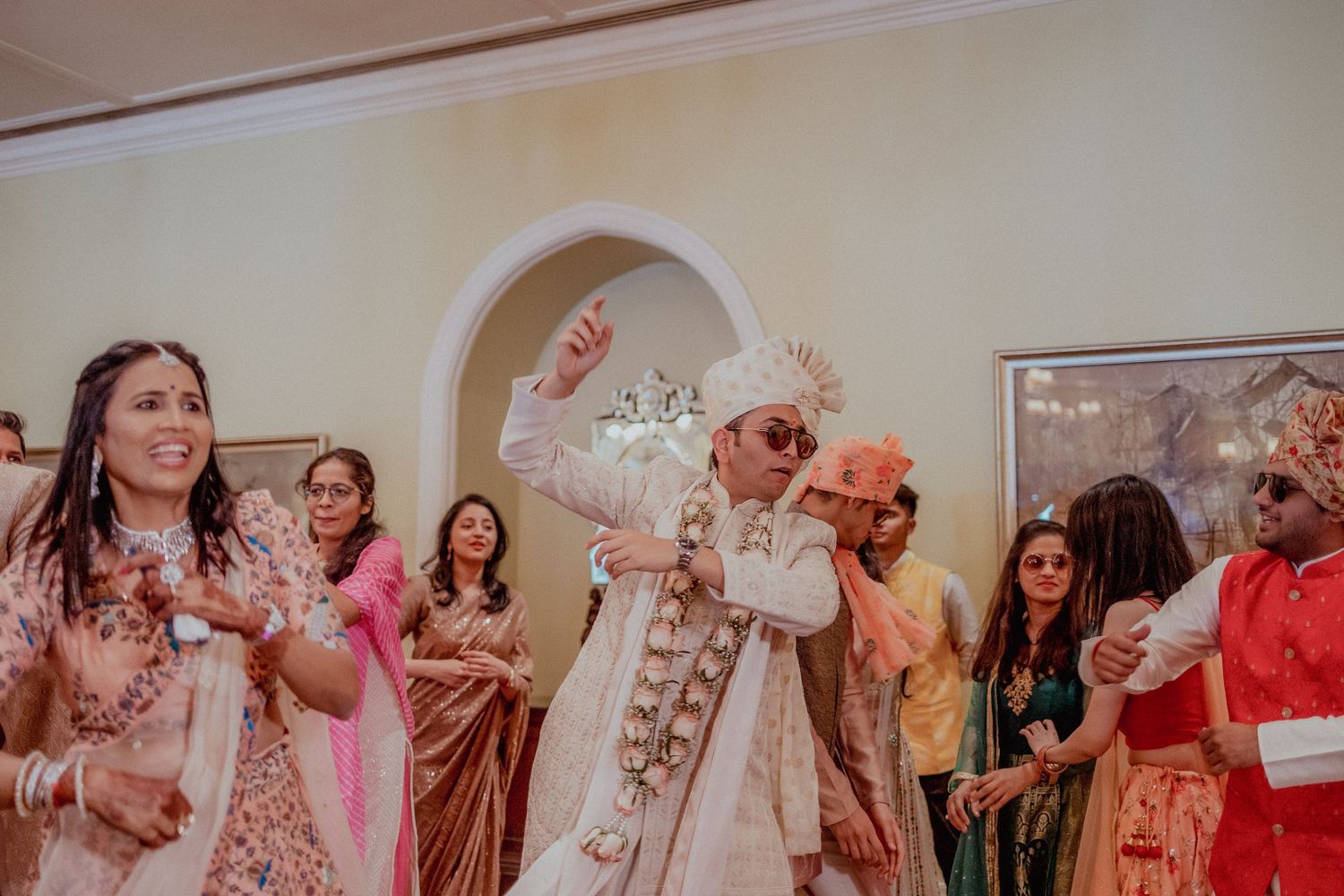 Groom in white sherwani and safa dances joyfully with guests at Indian wedding celebration.