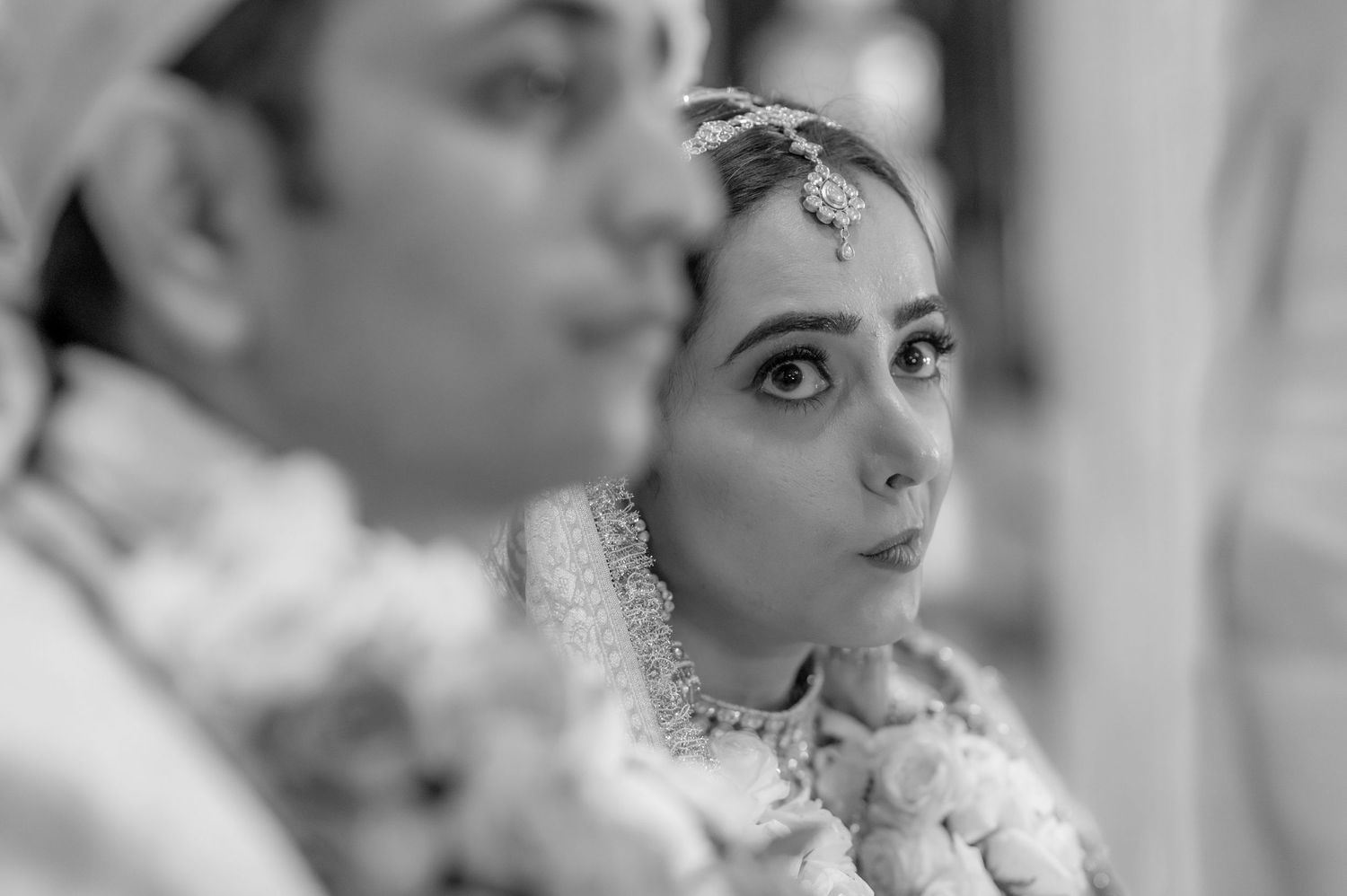 Black and white portrait of Indian bride with maang tikka gazing during wedding ceremony.