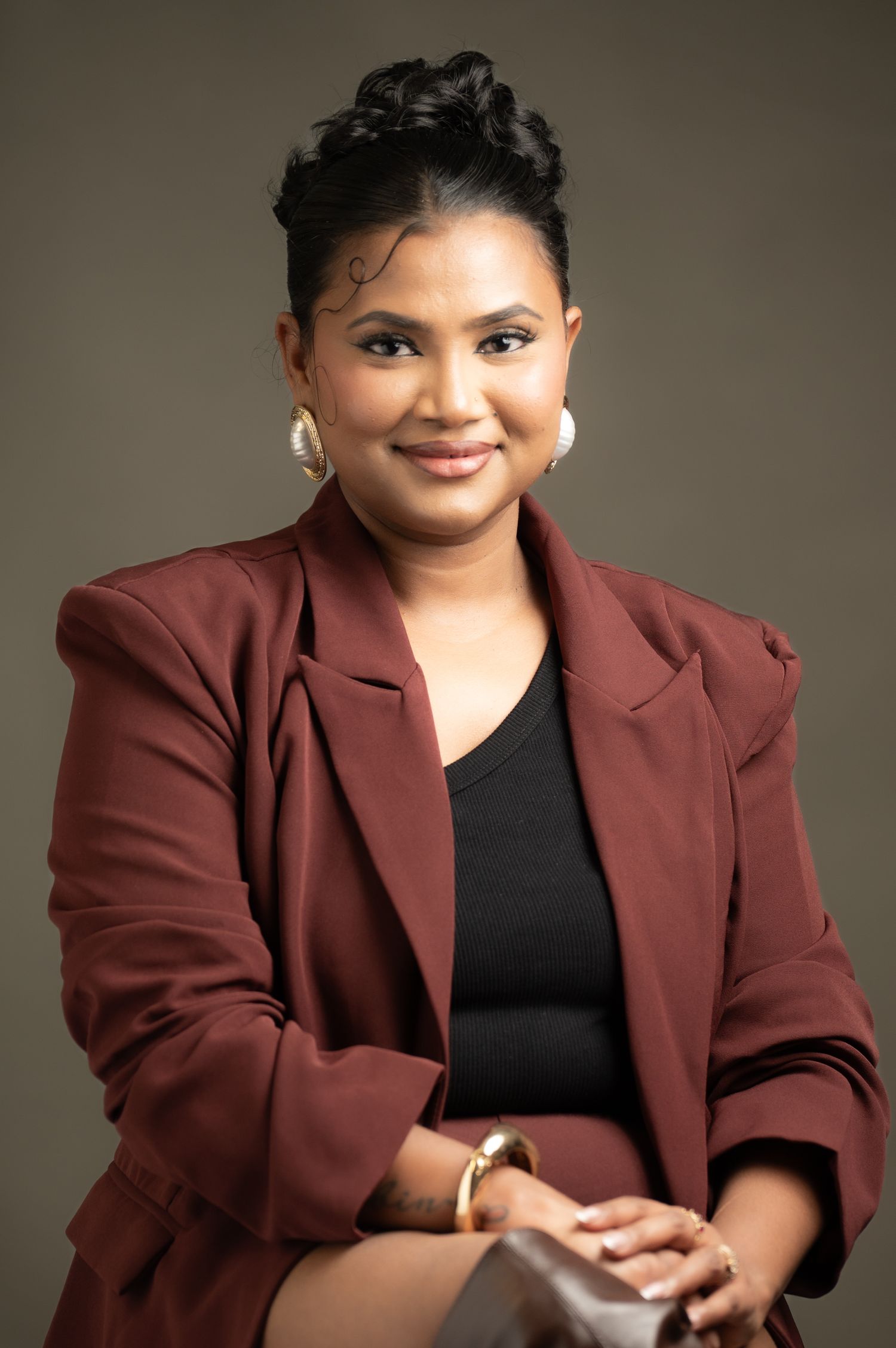 Woman in burgundy blazer and hoop earrings smiles confidently in professional studio portrait.